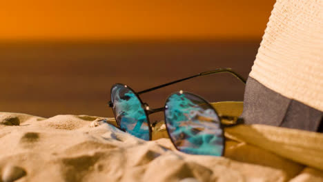 Sommerferienkonzept-Von-Strandtuch-Mit-Flip-flops,-Sonnenbrille-Und-Sonnenhut-Gegen-Sonnenunterganghimmel
