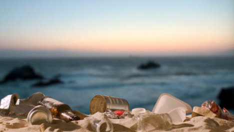 Pollution-Concept-With-Hand-Picking-Up-Bottles-And-Rubbish-On-Beach-Against-Sea-And-Sunset-Sky-Background