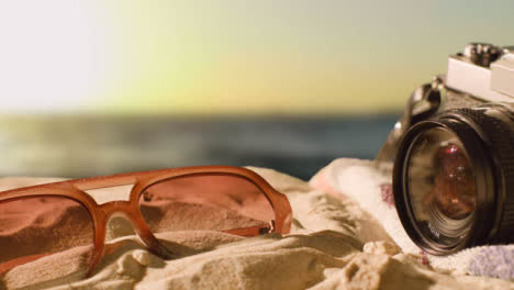 Sommerferienkonzept-Des-Strandtuchs-Mit-Sonnenbrille-Und-Kamera-Gegen-Sonnenunterganghimmel