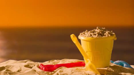 Summer-Holiday-Concept-With-Child's-Bucket-Spade-On-Sandy-Beach-Against-Sea-And-Sunset-Sky-1