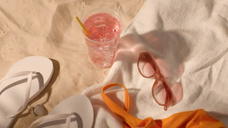 Summer-Holiday-Concept-Of-Cold-Drink-Sunglasses-Beach-Towel-Flip-Flops-Swimsuit-On-Sand