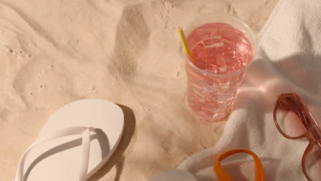 Summer-Holiday-Concept-Of-Cold-Drink-Sunglasses-Beach-Towel-Flip-Flops-Swimsuit-On-Sand-1