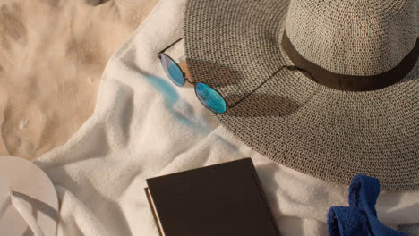 Summer-Holiday-Concept-Of-Sunglasses-Book-Beach-Towel-Flip-Flops-Hat-On-Sand-Background