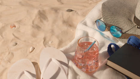 Summer-Holiday-Concept-Of-Cold-Drink-Sunglasses-Beach-Towel-Flip-Flops-Hat-Book-On-Sand