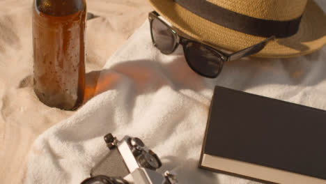 Sommerferienkonzept-Von-Bierflasche-Sonnenbrille-Strandtuch-Buch-Sonnenhut-Kamera-Auf-Sand-3