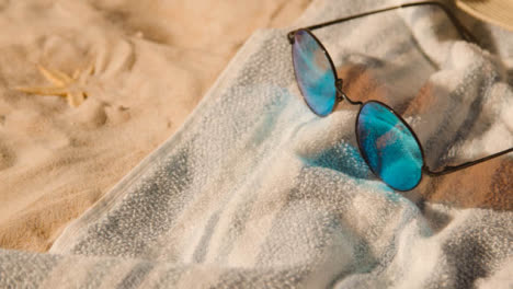 Concepto-De-Vacaciones-De-Verano-De-Gafas-De-Sol-Conchas-De-Toallas-De-Playa-Sobre-Fondo-De-Arena