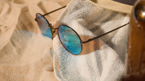 Summer-Holiday-Concept-Of-Beer-Bottle-Sunglasses-Beach-Towel-On-Sand-Background