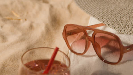 Summer-Holiday-Concept-Of-Cold-Drink-Sunglasses-Beach-Towel-Sun-Hat-On-Sand-Background-1