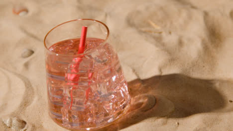 Summer-Holiday-Concept-Of-Cold-Drink-Book-Beach-Towel-Sun-Hat-On-Sand-Background