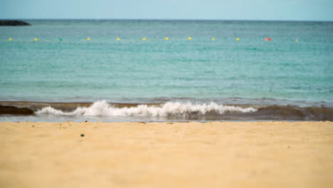 Person-Picking-Up-Bottle-Of-UV-Protection-Sun-Screen-Buried-In-Sand-On-Holiday-Beach-With-Sea-In-Background