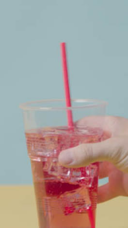 Vertical-Video-Summer-Holiday-Concept-With-Hand-Stirring-Cold-Drink-With-Ice-On-Yellow-Background-1