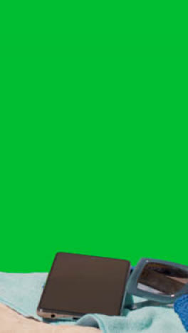 Vertical-Video-Summer-Holiday-Concept-Of-Sunglasses-Mobile-Phone-Beach-Towel-On-Sand-Against-Green-Screen