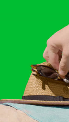 Vertical-Video-Summer-Holiday-Concept-Of-Sunglasses-Sun-Hat-Camera-Beach-Towel-On-Sand-Against-Green-Screen-1