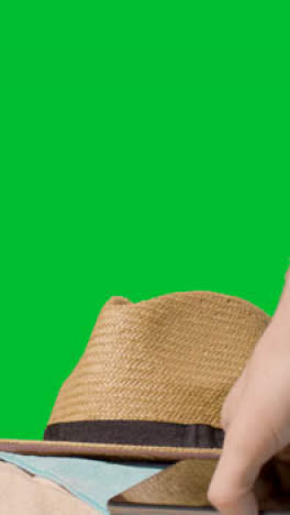 Vertical-Video-Summer-Holiday-Concept-Of-Sun-Hat-Mobile-Phone-Beach-Towel-On-Sand-Against-Green-Screen