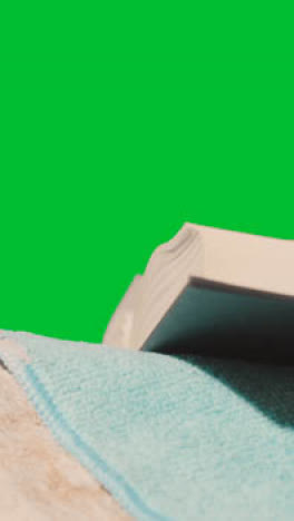 Vertical-Video-Summer-Holiday-Concept-Of-Person-On-Beach-Towel-Reading-Book-Against-Green-Screen