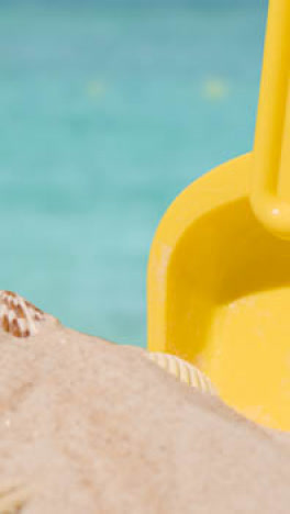 Vertical-Video-Summer-Holiday-Concept-With-Child's-Bucket-Spade-On-Sandy-Beach-Against-Sea-Background