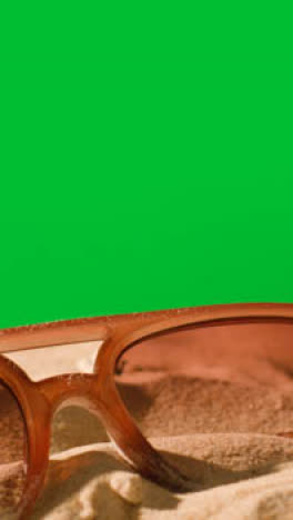 Vertical-Video-Summer-Holiday-Concept-Of-Sunglasses-On-Sand-Against-Green-Screen