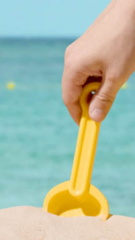 Vertical-Video-Summer-Holiday-Concept-With-Child's-Spade-On-Sandy-Beach-Against-Sea-Background