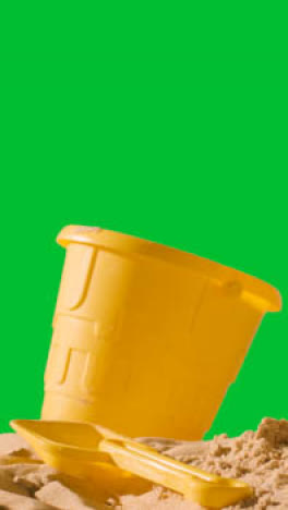 Vertical-Video-Summer-Holiday-Concept-With-Child's-Bucket-Spade-On-Sandy-Beach-Against-Green-Screen