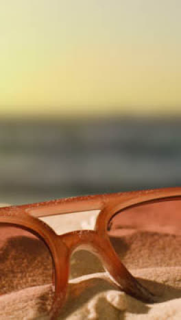 Vertikales-Video-Sommerferienkonzept-Mit-Sonnenbrille-Am-Sandstrand-Gegen-Meer-Und-Abendhimmel