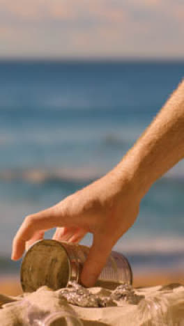 Vertical-Video-Of-Pollution-Concept-With-Hand-Picking-Up-Litter-And-Rubbish-On-Beach-Against-Sea-Background