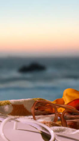 Vertical-Video-Summer-Holiday-Concept-Of-Beach-Towel-With-Flip-Flops-Sunglasses-And-Sun-Hat-Against-Sunset-Sky