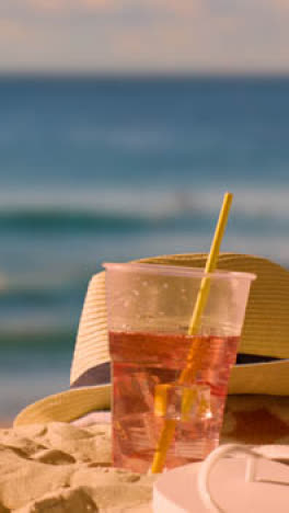 Vertical-Video-Summer-Holiday-Concept-Of-Cold-Drink-On-Beach-Towel-With-Sun-Hat-Against-Evening-Sky