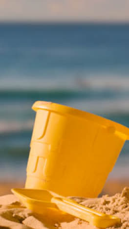 Vertikales-Video-Sommerferienkonzept-Mit-Eimerspaten-Für-Kinder-Am-Sandstrand-Vor-Abendlichem-Meereshintergrund