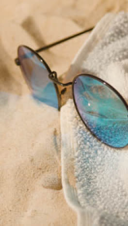 Vertical-Video-Summer-Holiday-Concept-Of-Sunglasses-And-Beach-Towel-On-Sand