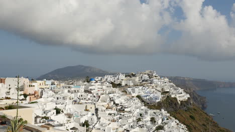 Grecia-Santorini-Fira-Ciudad-Bajo-Una-Nube-Con-Pájaros-Volando