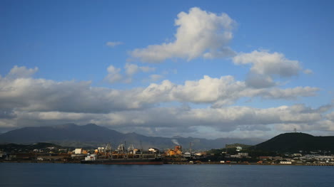 Nueva-Caledonia-Cúmulos-Se-Elevan-En-El-Cielo-Azul-Sobre-Las-Plantas-Industriales-Frente-Al-Mar
