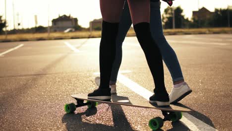 Back-View-Of-Young-Attractive-Hipster-Girl-Being-Taught-Skateboarding-By-A-Friend-Who-Is-Supporting-Her-Holding-Her-Hand