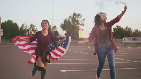 Junge-Glückliche-Amerikanische-Hipster-mädchen,-Die-Laufen,-Während-Sie-Die-Amerikanische-Flagge-Halten-Und-Rauchbombengranate-Mit-Weißer-Farbe-Ablassen,-Die-Spaß-Haben