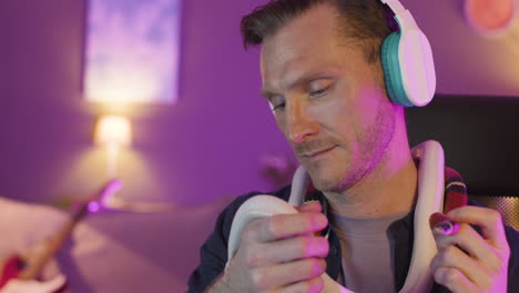 Close-Up-View-Of-Man-In-Headphones-Sitting-At-Desk-While-Petting-And-Holding-Two-Snakes-Around-His-Neck