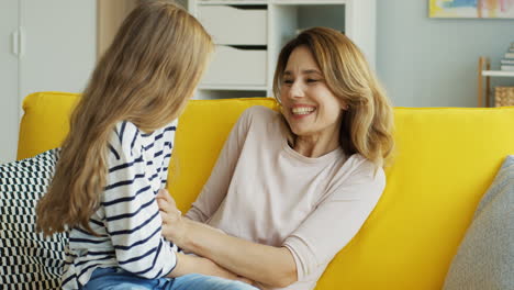Beautiful-Mother-And-Teenager-Daughter-Having-Fun-On-Yellow-Sofa-And-Tickling-In-The-Living-Room