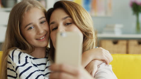 Close-Up-View-Of-Mother-And-Cute-Girl-Taking-A-Selfie-With-Smartphone-Sitting-On-Sofa-In-Living-Room-1