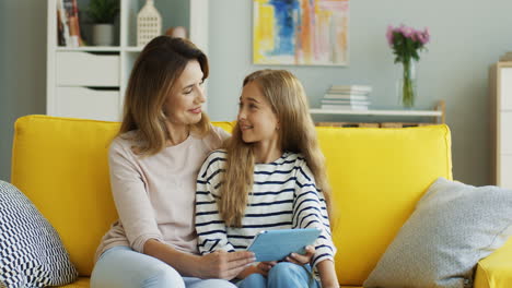 Blonde-Mother-And-Daughter-Resting-On-The-Sofa-At-Home-And-Watching-Something-On-Tablet-1