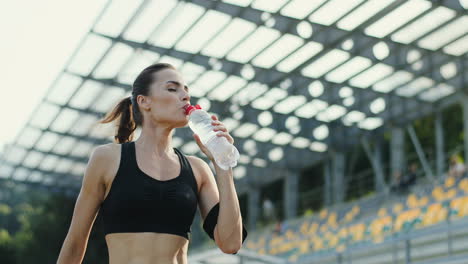 Junge-Joggerin,-Die-An-Einem-Sommermorgen-Im-Stadion-Trainiert-Und-Wasser-Aus-Einer-Flasche-Trinkt