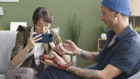 Couple-Holding-Pet-Snakes-Sitting-On-A-Comfortable-Sofa-At-Home