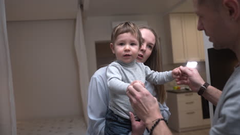 Madre-Sosteniendo-A-Su-Bebé-En-Brazos-En-La-Sala-De-Estar-De-Casa-Mientras-Su-Padre-Le-Tomaba-Las-Manos