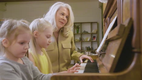 Zwei-Kleine-Mädchen-Spielen-Zu-Hause-Altes-Klavier,-Während-Ihre-Großmutter-Neben-Ihnen-Sitzt