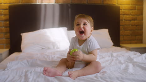 Vorderansicht-Eines-Babys,-Das-Auf-Dem-Bett-Im-Schlafzimmer-Sitzt,-Während-Es-In-Einen-Grünen-Apfel-Beißt-1
