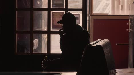 Silhouette-Of-Adult-Man-Sat-On-Bench-Indoors-With-Traffic-Going-Past-Outside