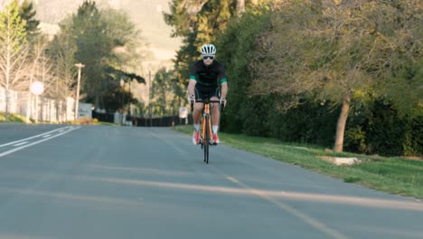 Tracking-Shot-of-a-Young-Male-Cyclist-Casually-Pedaling-Down-a-Road