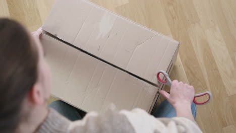 Young-woman-cuts-postal-parcel-open-with-scissors-and-opens-the-cardboard-box