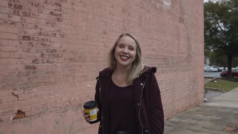 Slow-Motion-Shot-of-a-Young-Female-Smiling-and-Walking-Down-the-Street-with-a-Coffee-Cup-in-Hand