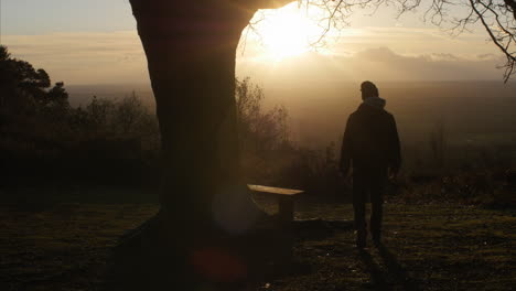 Una-Toma-Estática-De-Un-Hombre-Caminando-Hacia-Un-Banco-Y-Sentándose-Con-Una-Hermosa-Vista-Al-Amanecer