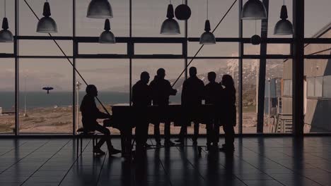 Silhouettes-Of-Backlit-Singers-With-Pianist-Inside-Room-With-Large-Glass-Windows