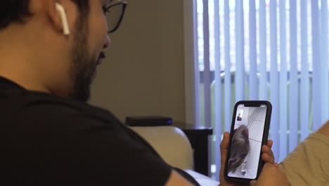 Young-Latino-man-looking-at-his-cat-on-the-phone-and-connecting-with-his-family-via-face-time