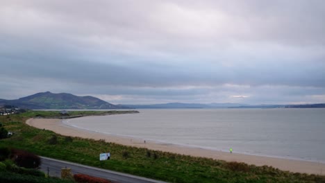 Windy-Northern-Ireland-coastal-shoreline-timelapse,-people-moving-on-beach-over-fast-moving-coastline-traffic